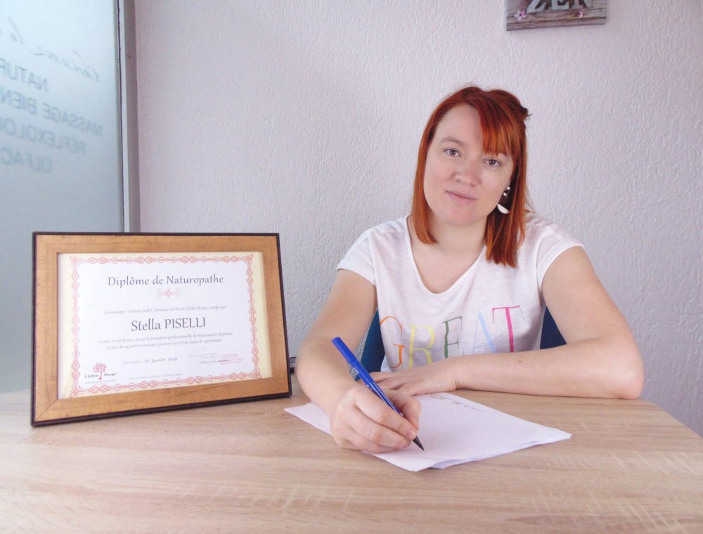 photo d'une jeune femme assis à un bureau à côté d'un diplôme de naturopathe